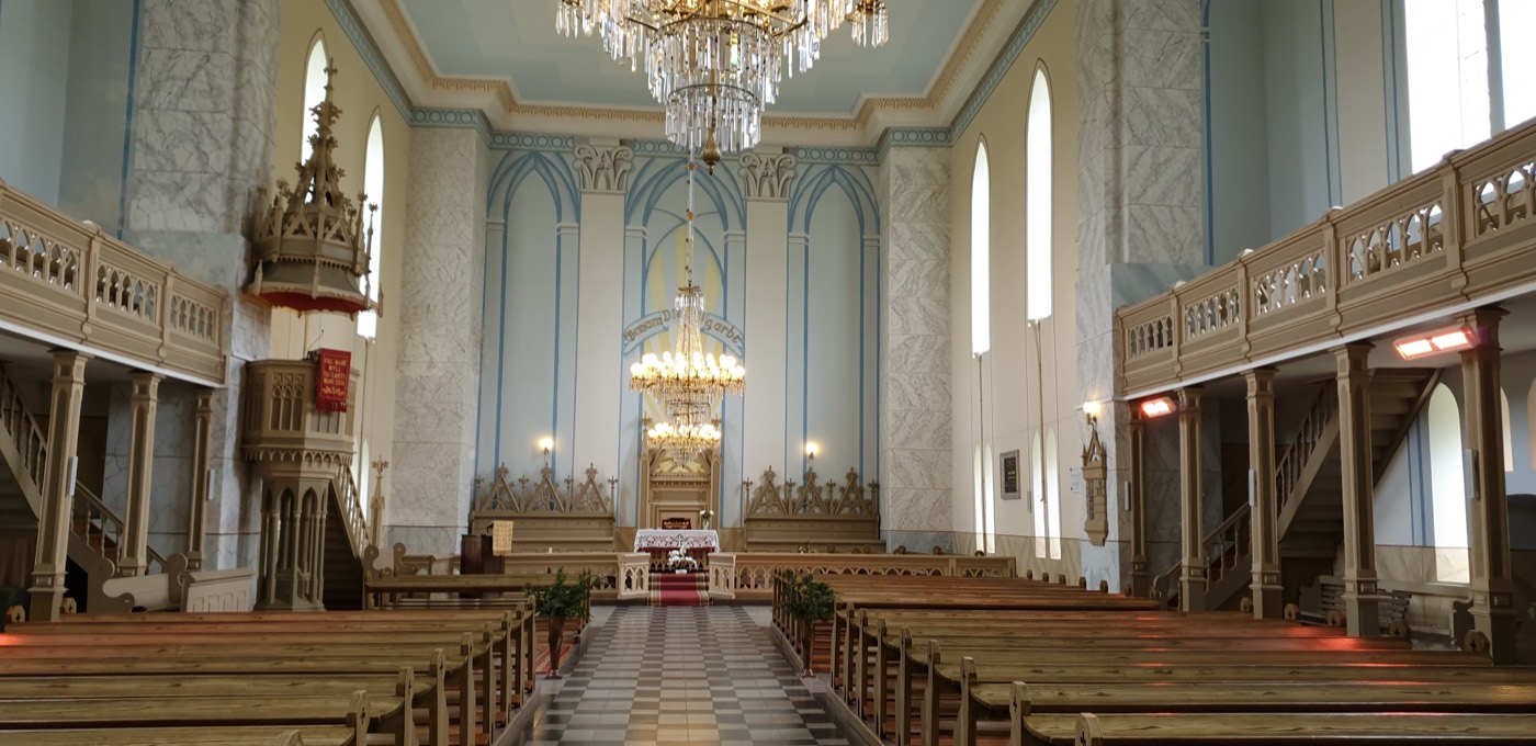 Biržų evangelikų reformatų bažnyčios vidus: mediniai suolai, sakykla, balkonai ir krištolo sietynai šviesiai mėlynoje erdvėje